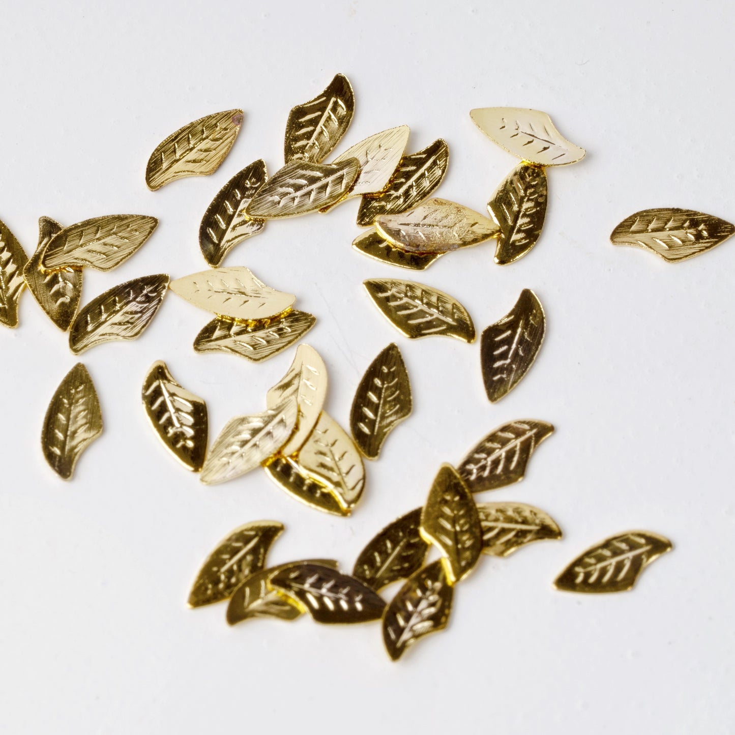 Gold leaf nail charms scattered on a white background.