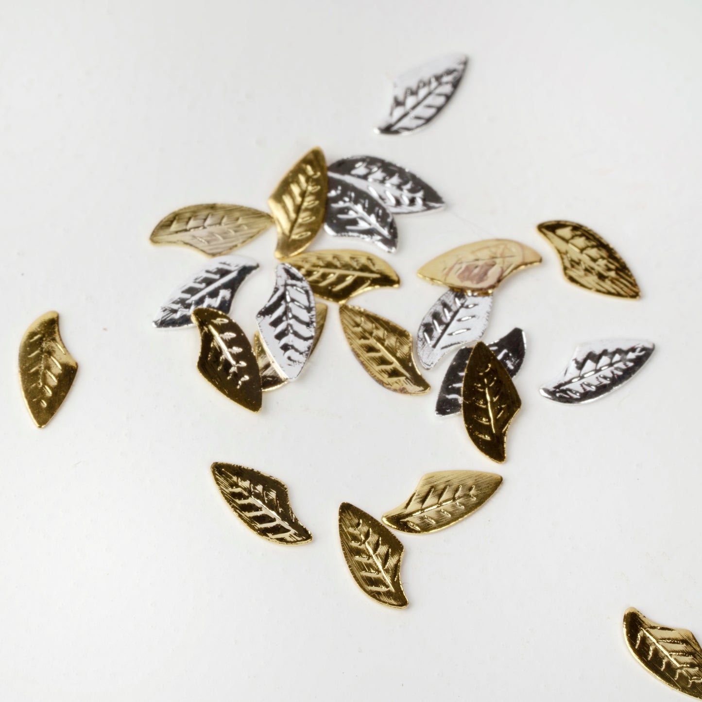 Gold and silver leaf nail charms scattered on a white background.