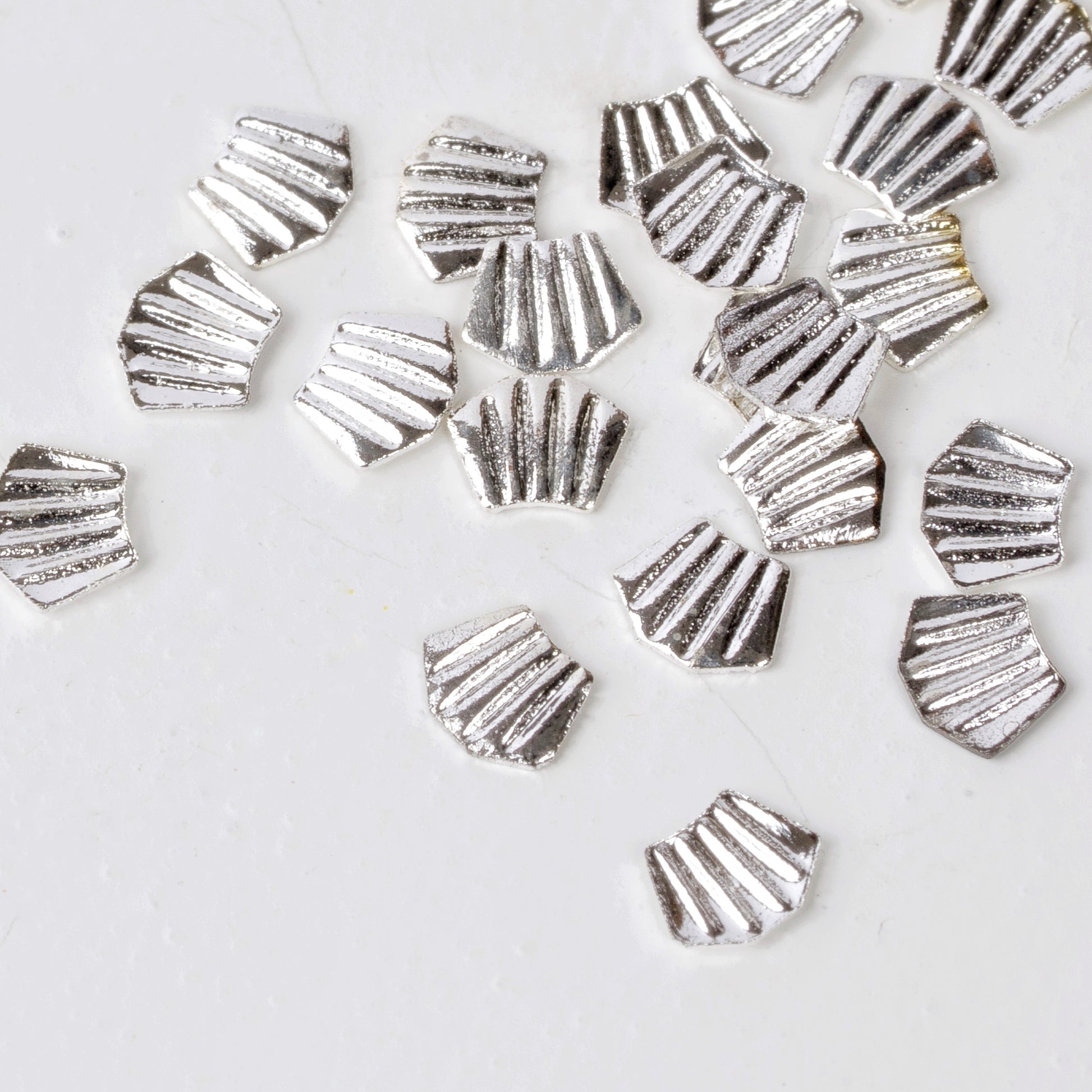 Silver nail charms scattered on white background.