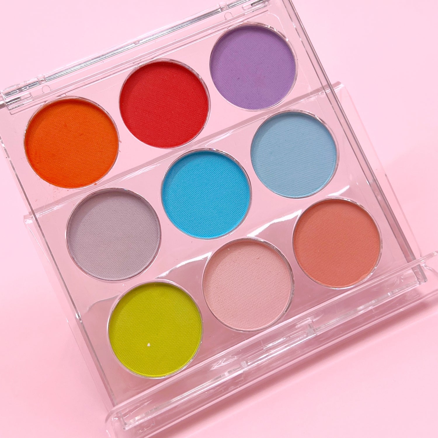 Mutlicolor pigment palette in clear case on pink background. 