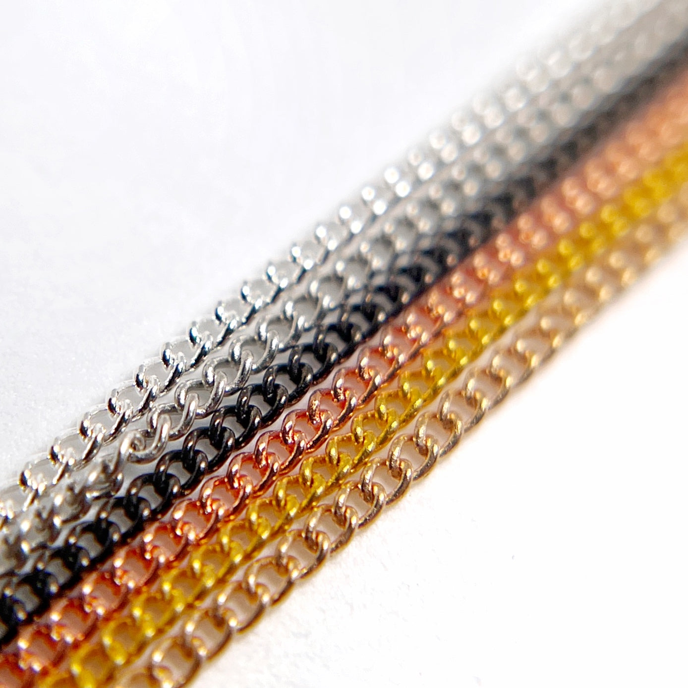 Close-Up of Multi-Color Nail Art Chains in metallic tones on White Background.