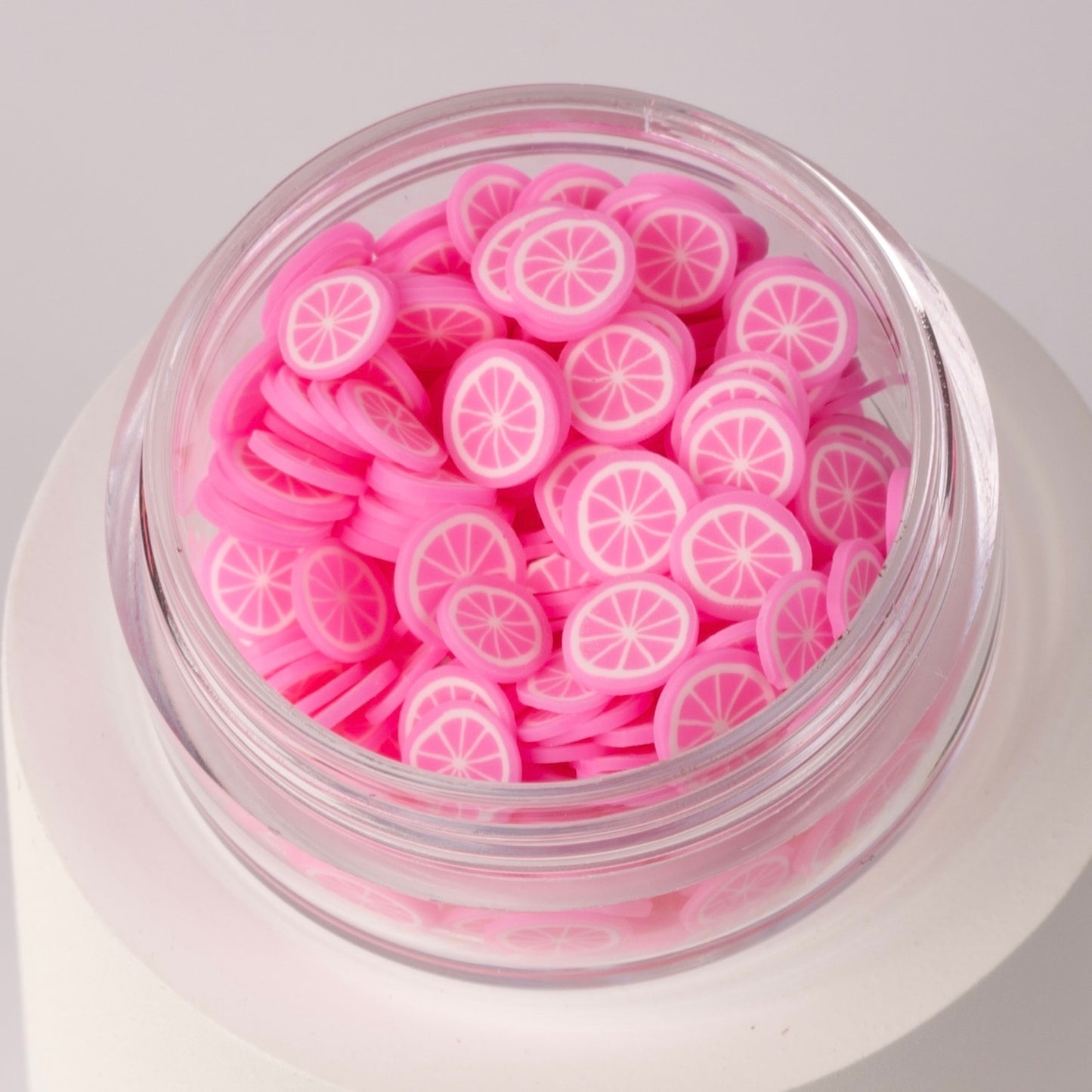 Mini pink lemon slices in clear jar on white background.