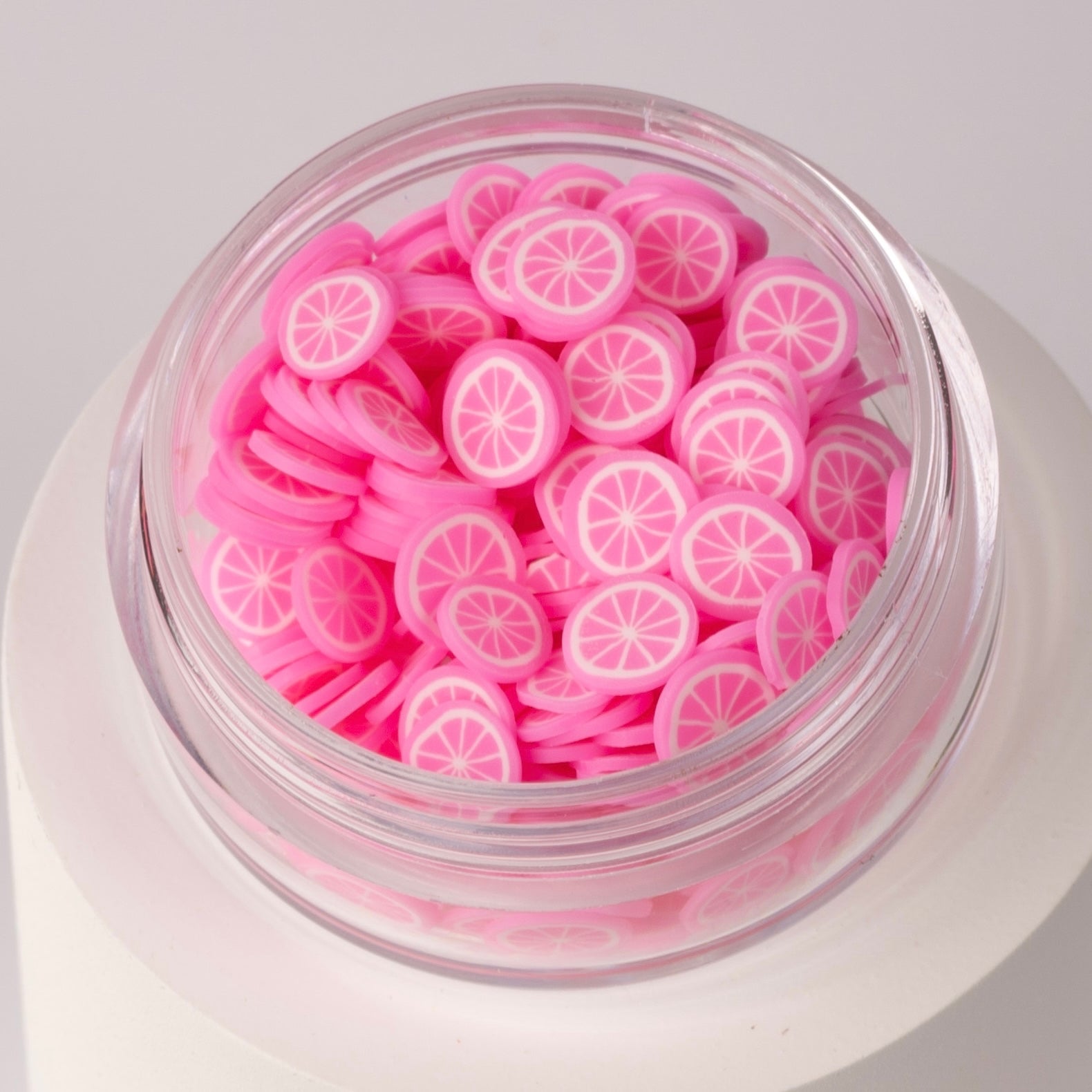 Mini pink lemon slices in clear jar on white background.