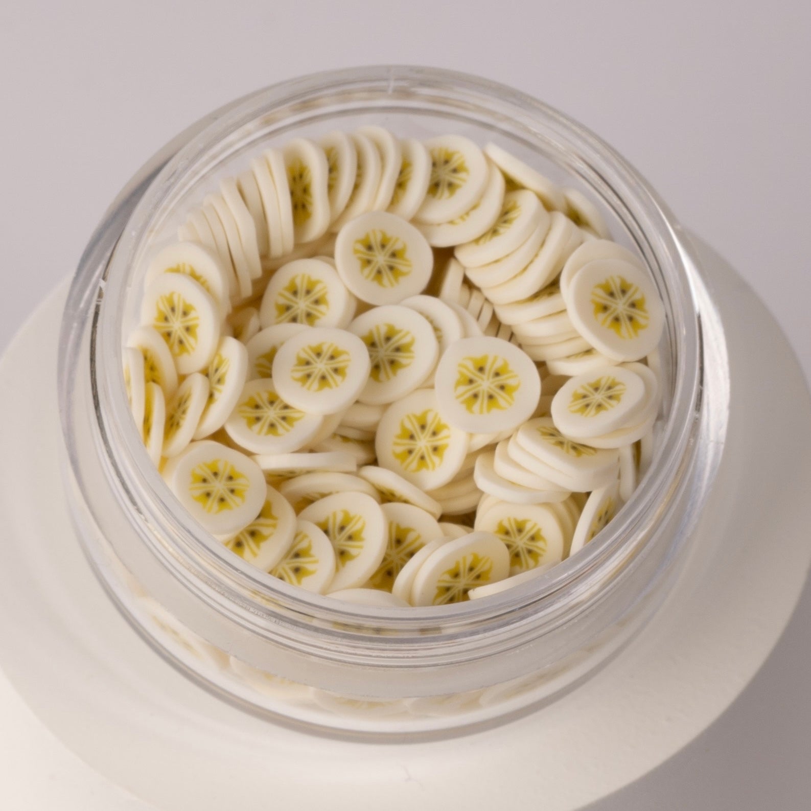 Mini banana slices in clear jar on white background.