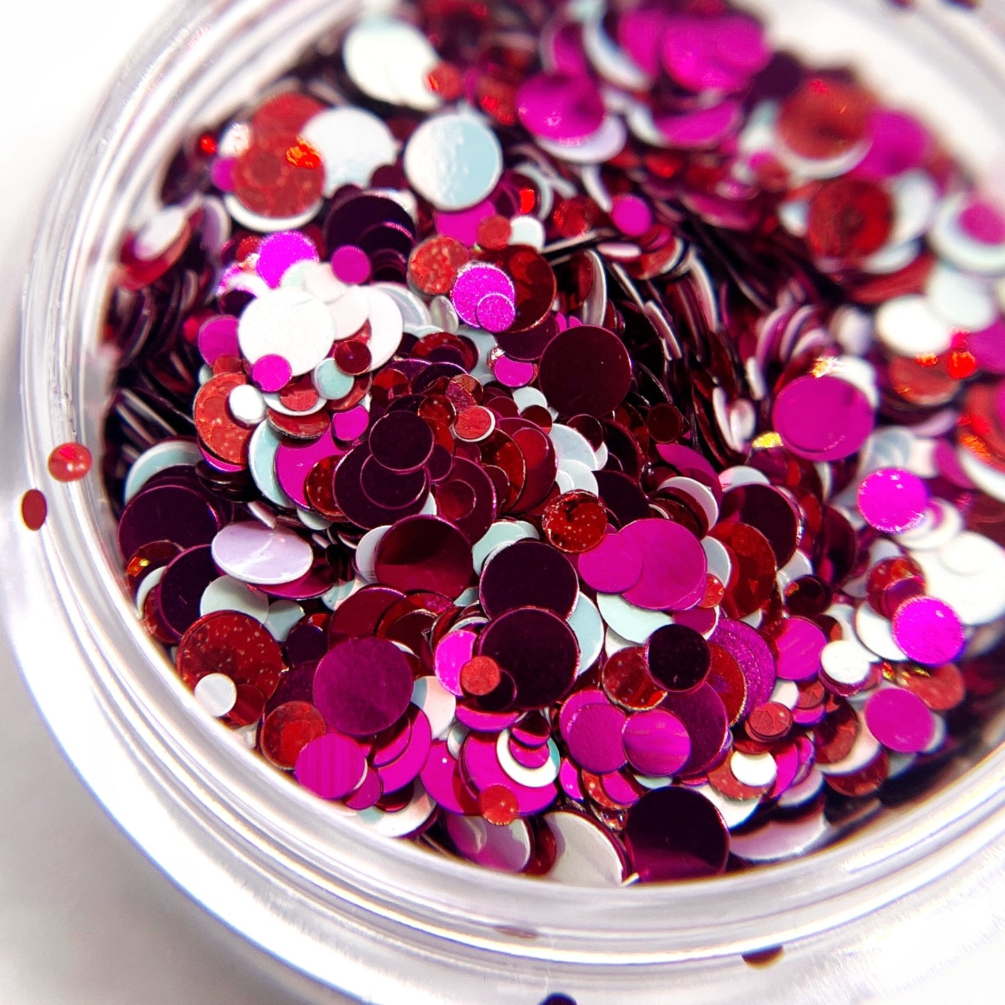 Multicolor and multi-size circle gittler mix in pink, red and white in a clear jar on a white background. 