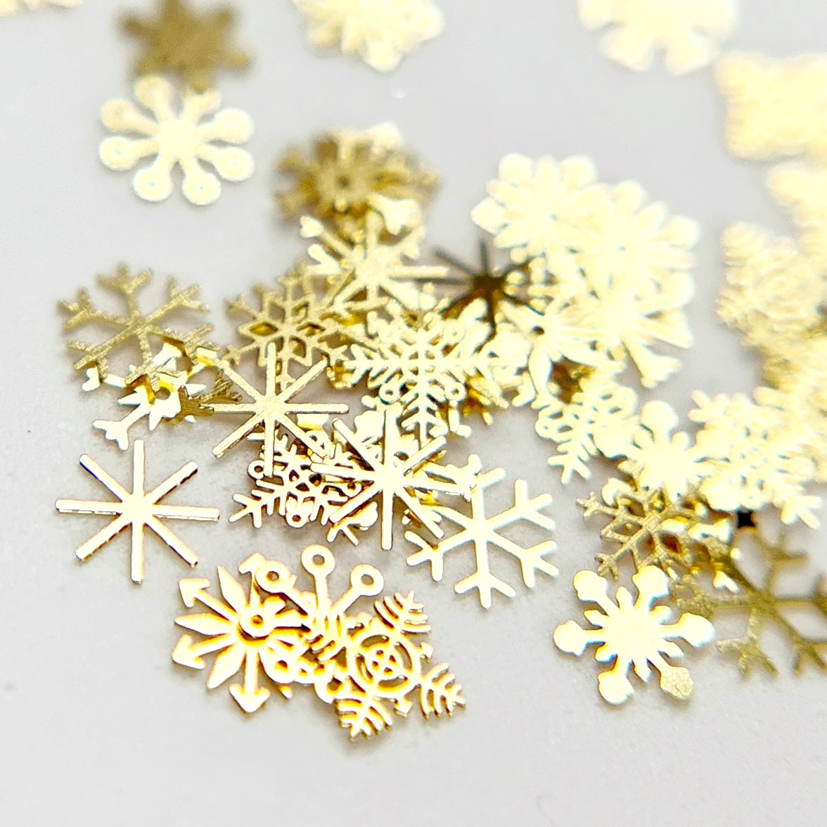 Snowflake Slice - Thin Gold Metal Snowflake Nail Charm, Presented on White Background.