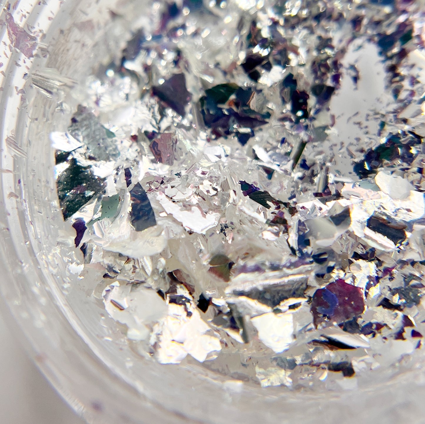 Detailed view of silver flakes in clear jar on white backgroud. 