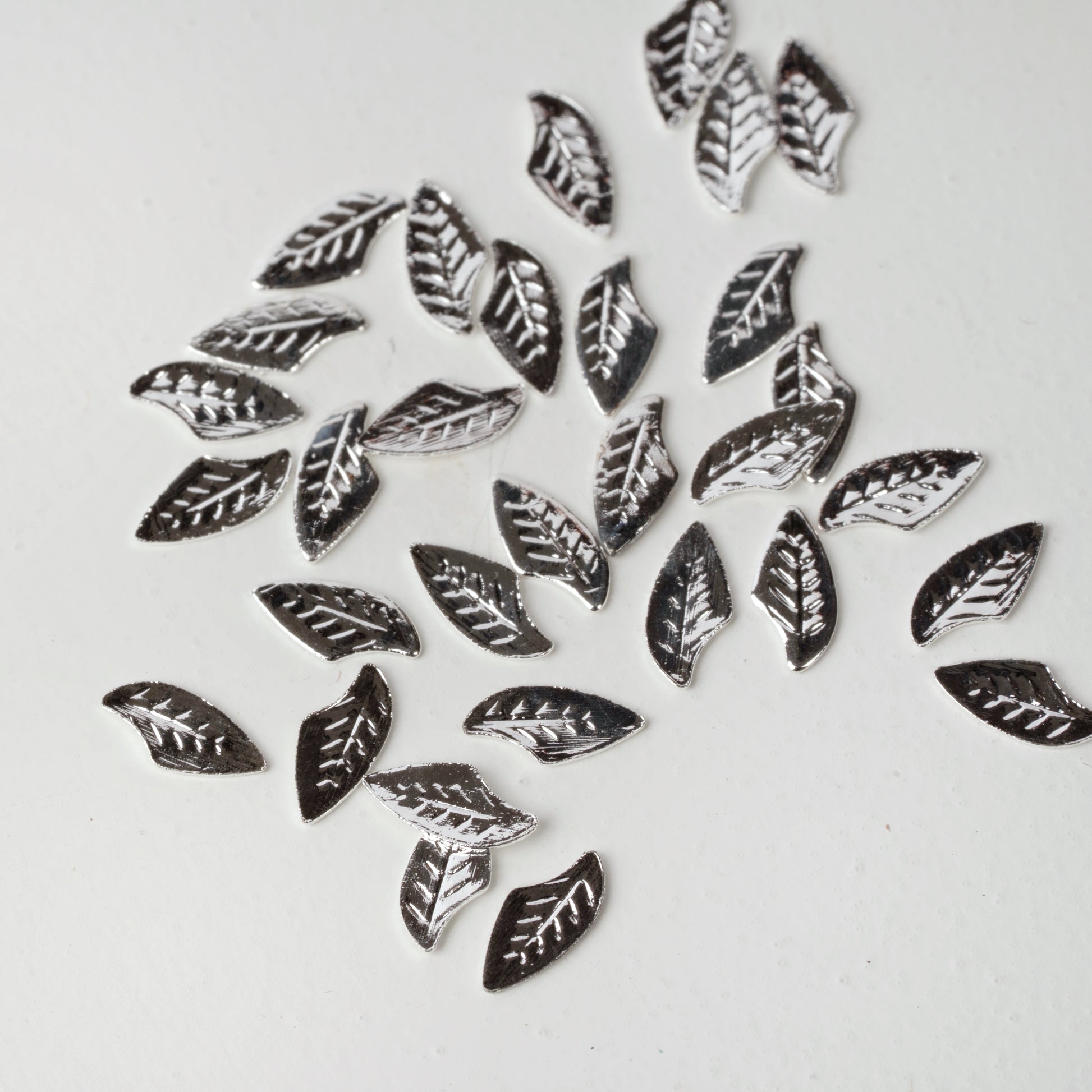 silver leaf nail charms scattered on a white background.