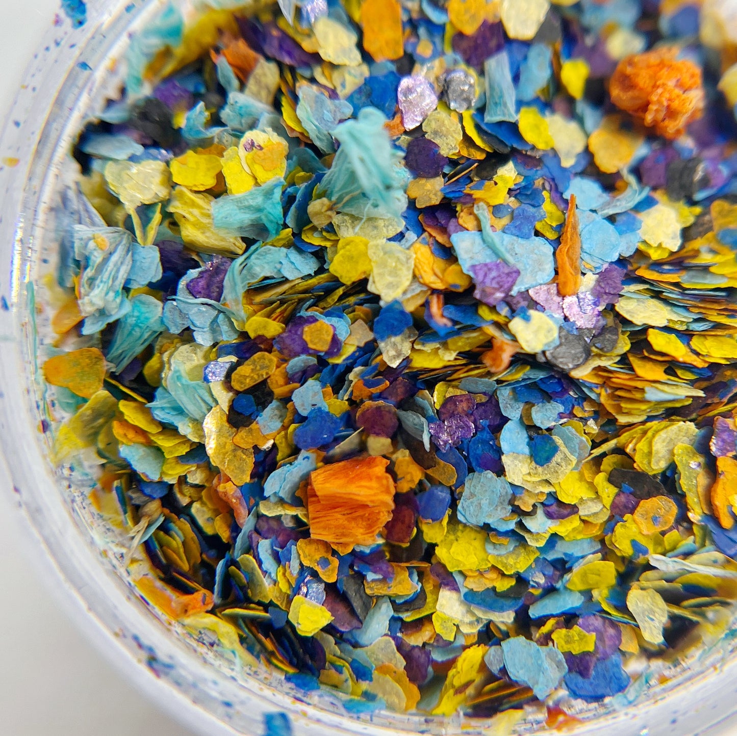 Confetti Crush Collection in Azure Crush- Colorful Mix of Mica Speckles and Dried Flower Petals in Jar, Featuring Blue, Yellow, Orange and Purple on White Backgroud. 