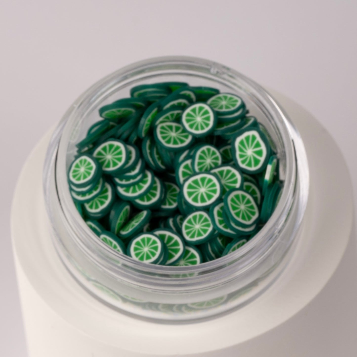 Mini lime slices in clear jar on white background.