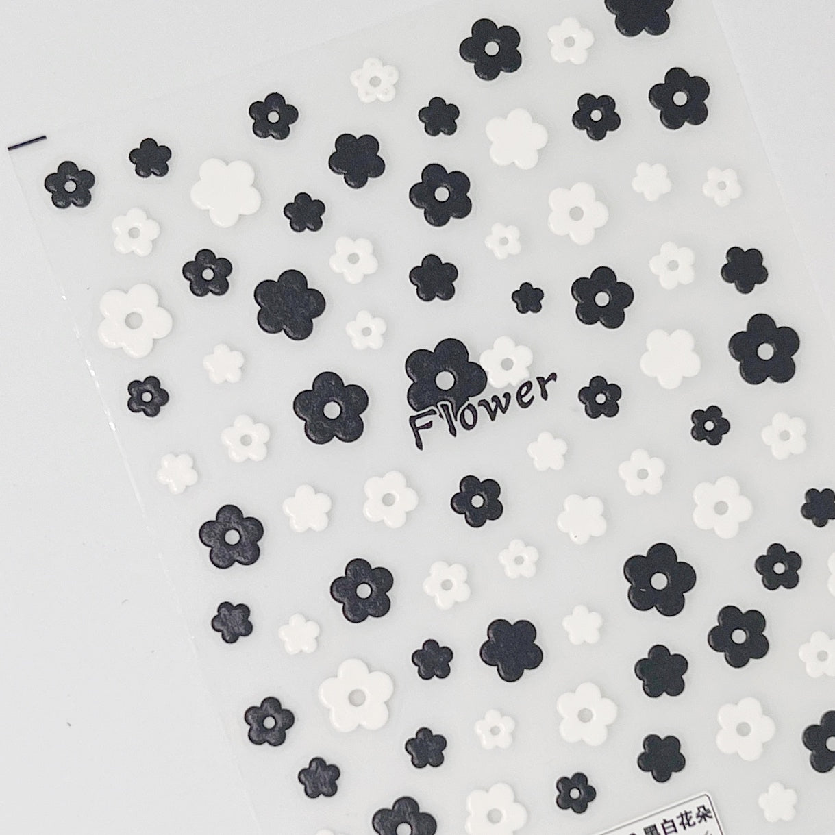 Black and white flower nail stickers on clear sheet placed on white background. 