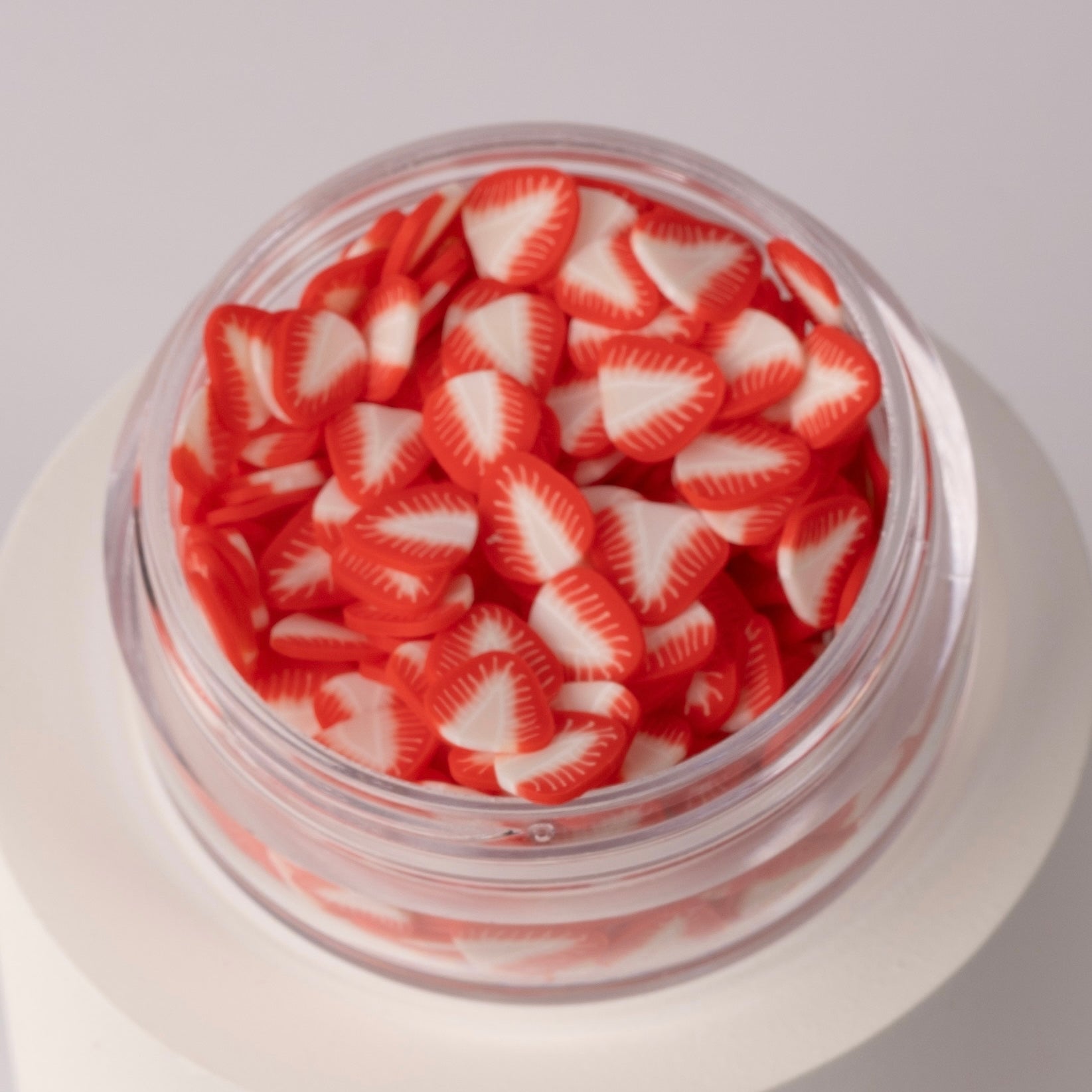 Mini strawberry slices in clear jar on white background.