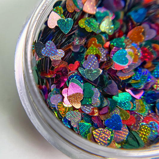 Cloce up of multi-color heart glitter in clear jar on white background. 