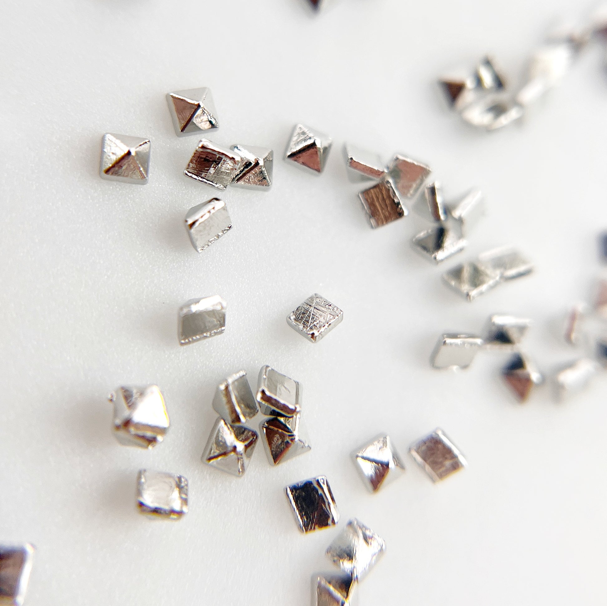 Silver pyramid studs scattered on white background. 