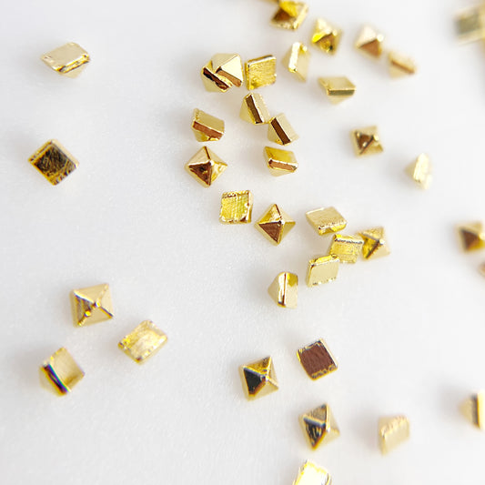 Small gold pyramid charms scattered on white background. 