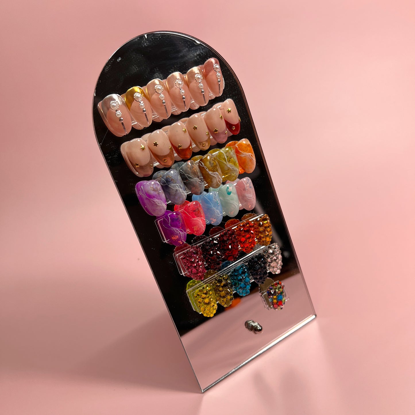 Photo of mirrored nail art display wth tips on pink backdrop. 