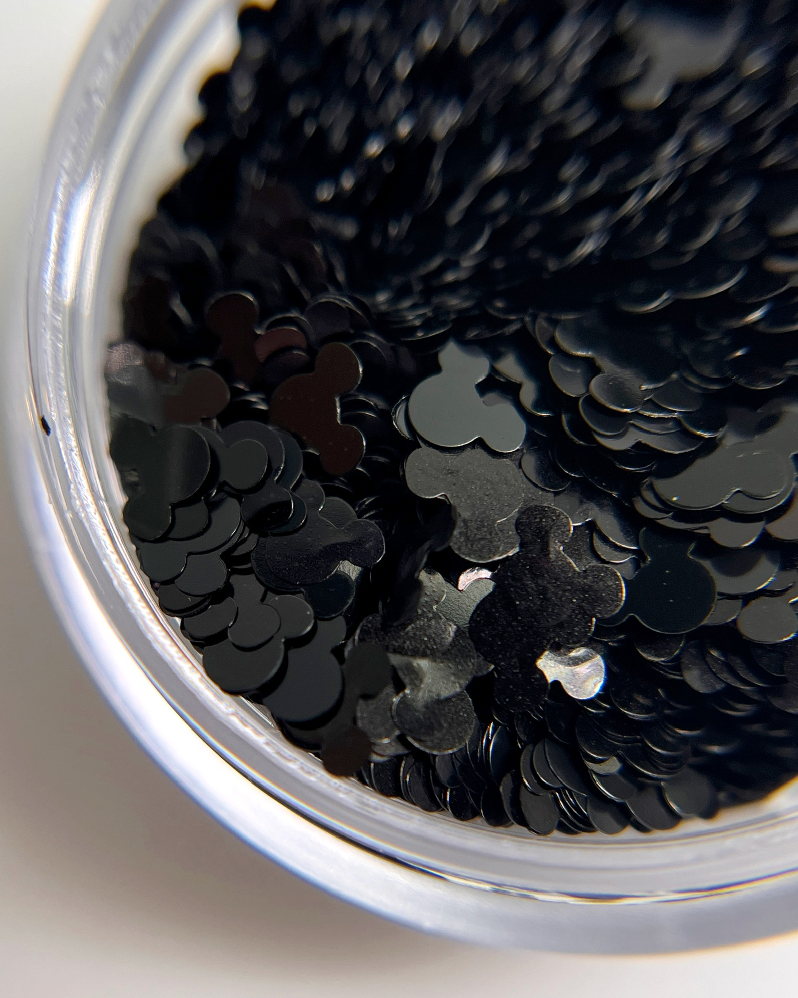 Black mouse shaped glitter in a clar jar on a whie background.