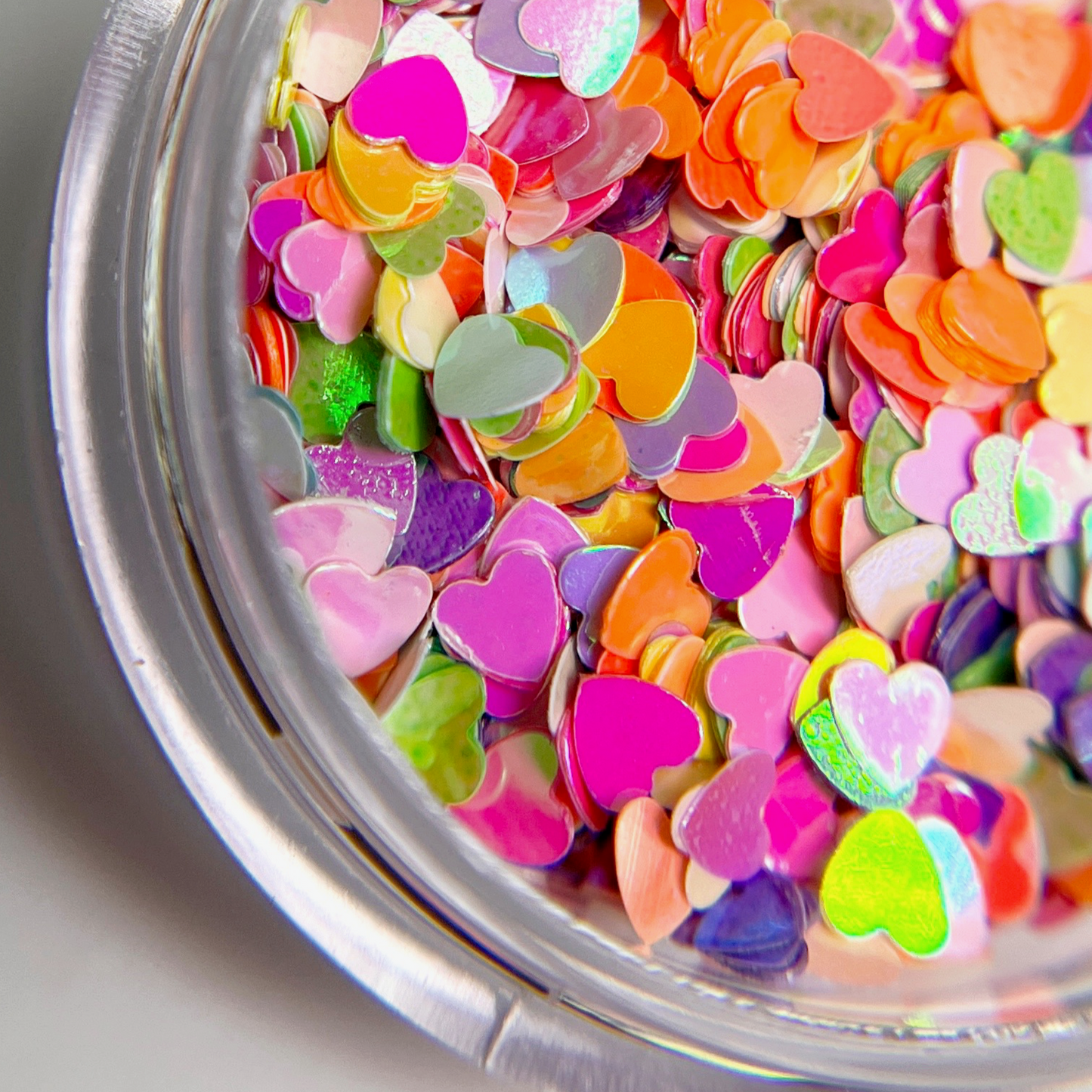 Detail view of multicolor heart shaped glitter in clear jar on white background. 