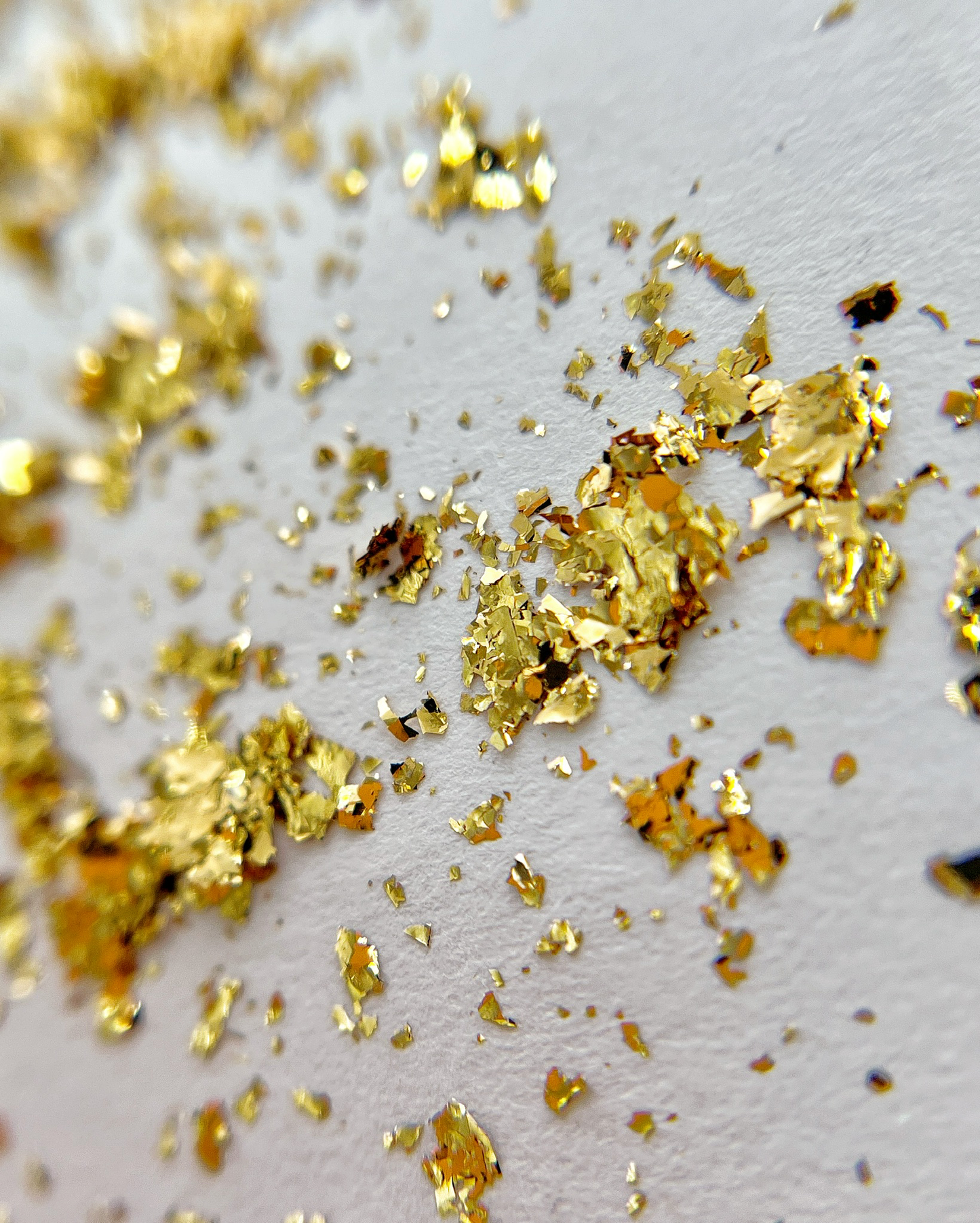 Thin gold foil flakes scattered on white background. 