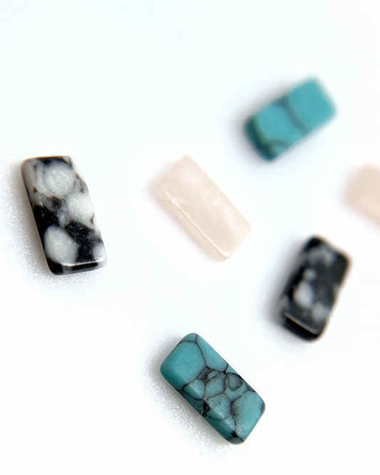 Mix of stone nail charms scattered on white background.