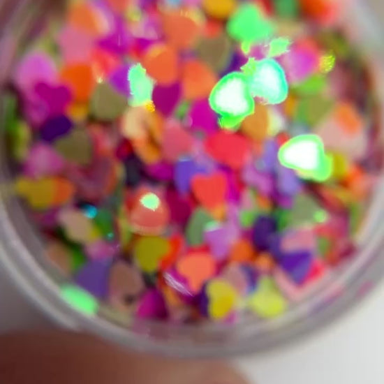 Video of hand holding jar of multicolored heart shaped glitter. 