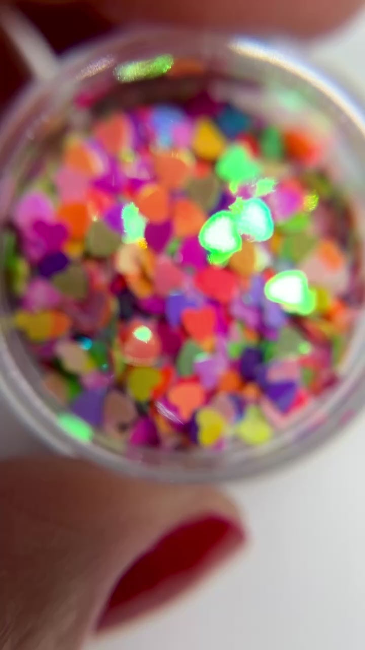 Video of hand holding jar of multicolored heart shaped glitter. 
