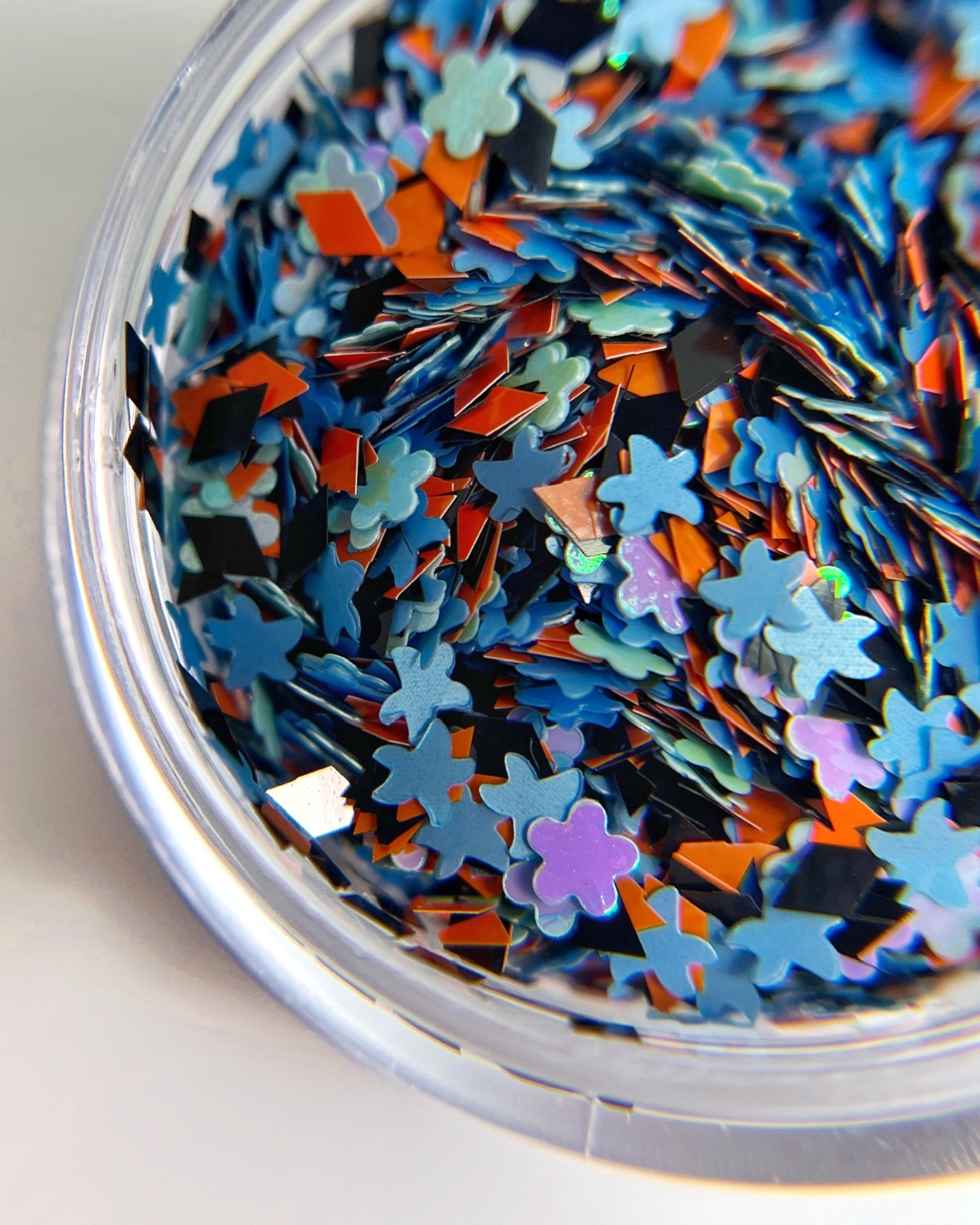 Detail view of multi shaped glitter in clear jar on white background. 